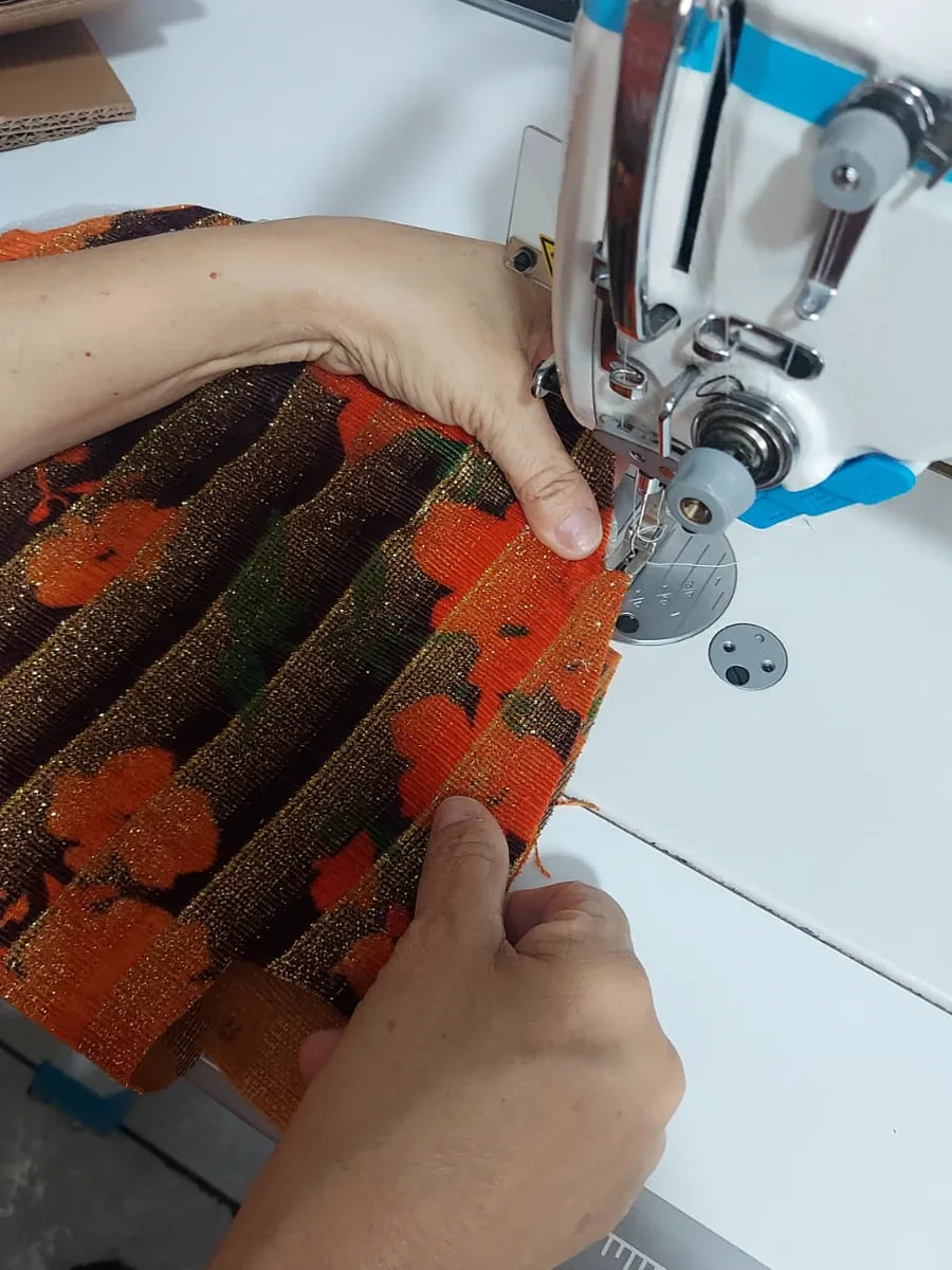 Mãos costurando à máquina o tecido de uma bolsa KABU no ateliê